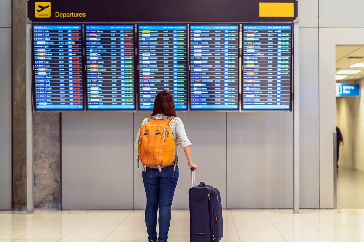 Traveler with luggage reading a flight information screen inside an airport