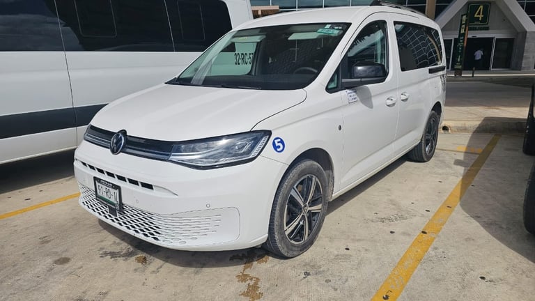 White Volkswagen ID.Buzz electric van parked in a lot, front three-quarter view showing LED headlights and charging port