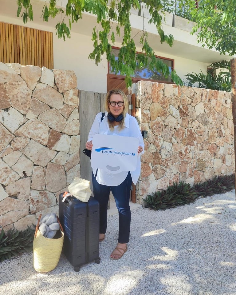 Traveler with luggage holding a TTC welcome sign outside a Tulum hotel property
